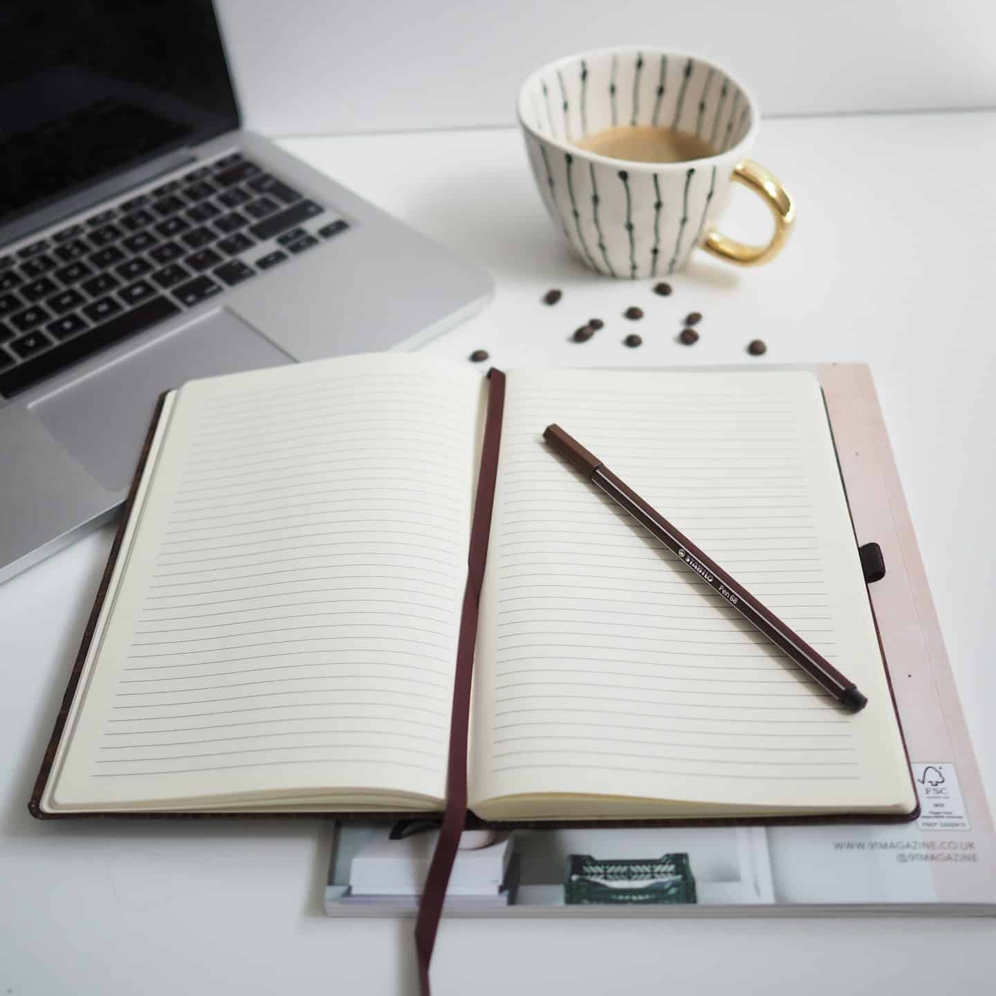 Overhead view of a minimalist desk with a laptop, notebook, and coffee cup.